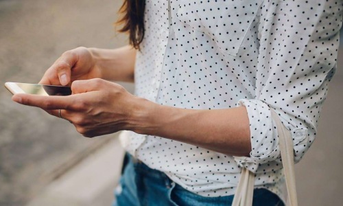 woman walks down the street and texts with a bag of groceries on her arm